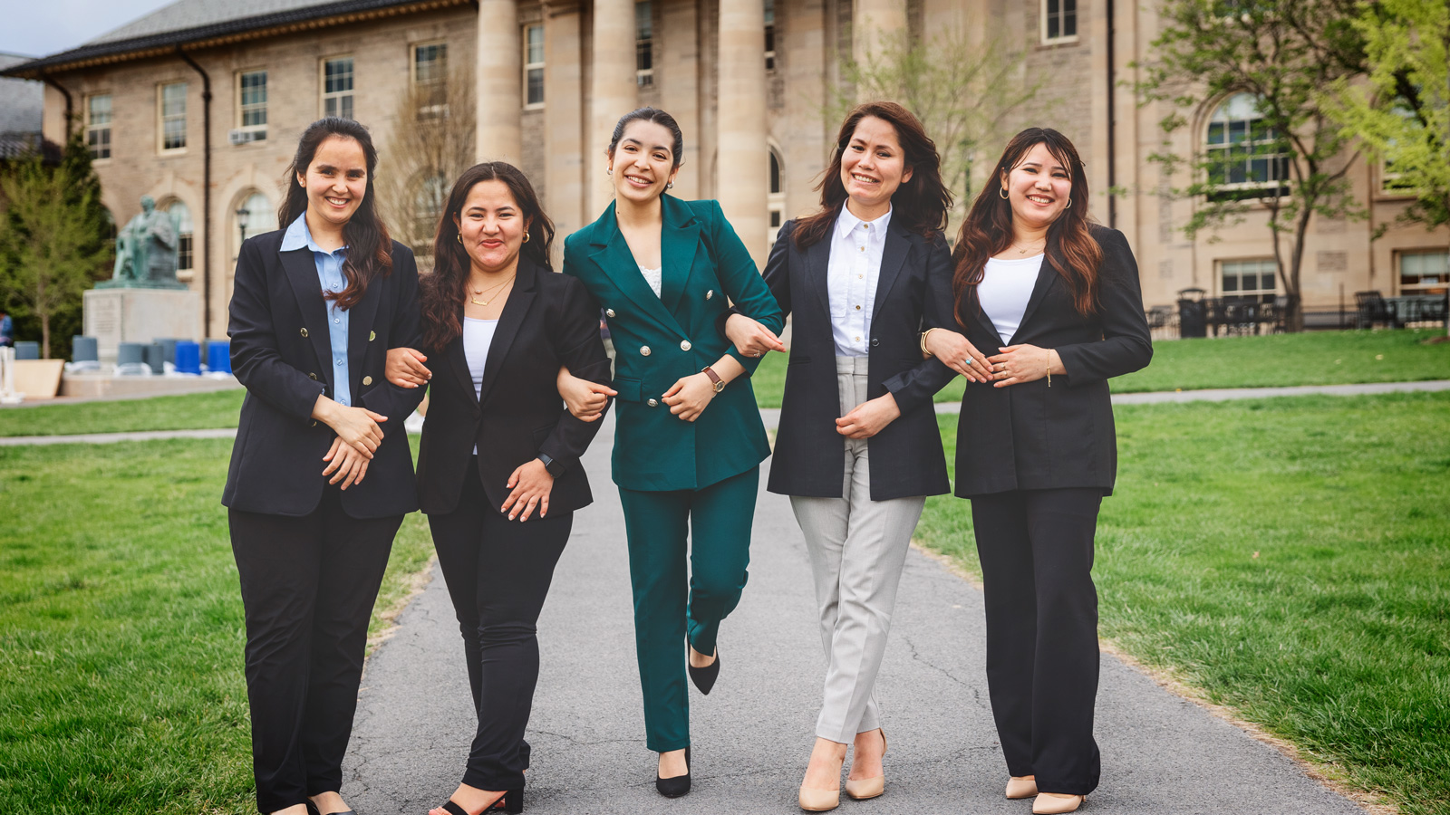 Tamana Ghaznawi, Simah Gul Sahnosh, Diana Ayubi, Khadija Monis, and Khurshid Hussainy walk through the Arts Quad while smiling and locking arms.