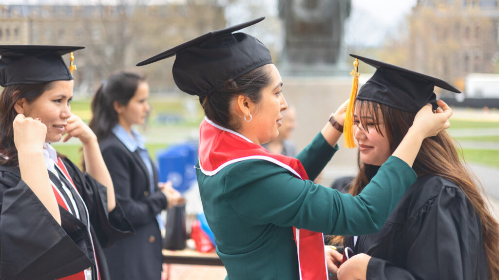 Diana Ayubi wears her graduation cap and stole while helping adjust Khurshid Hussainy's cap on the Arts Quad.