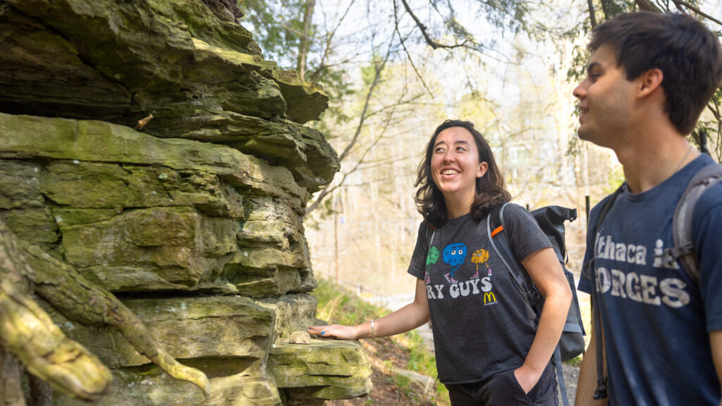 Two students smile and admire the rock structure in front of them during a hike in the woods at Beebe Lake.