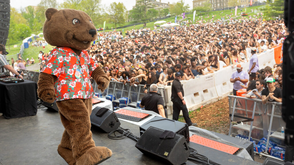 Touchdown in a tropical shirt on stage with a large crowd of students in the background.