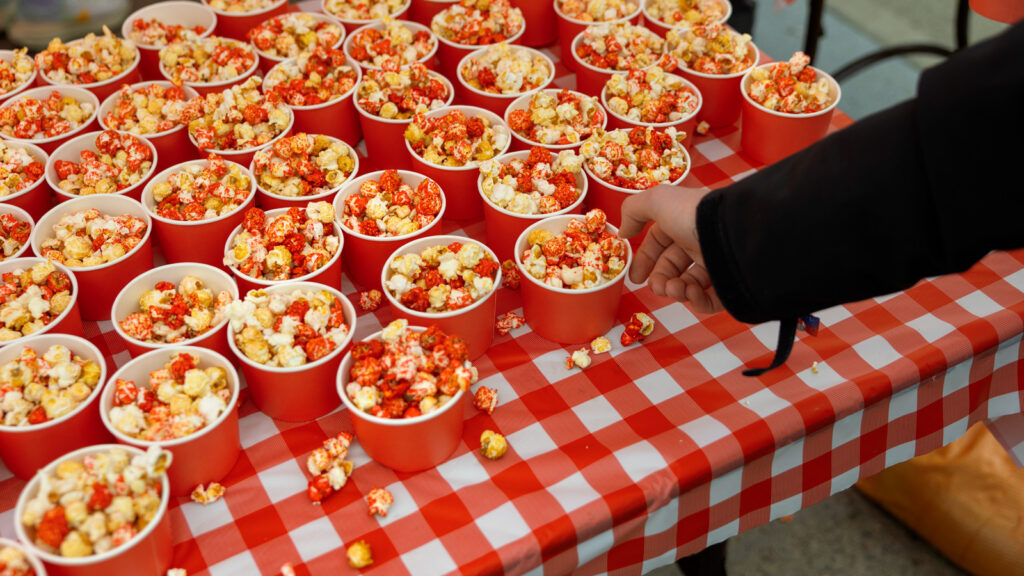 Dozens of popcorn cups on a table with a hand reaching in to grab one.