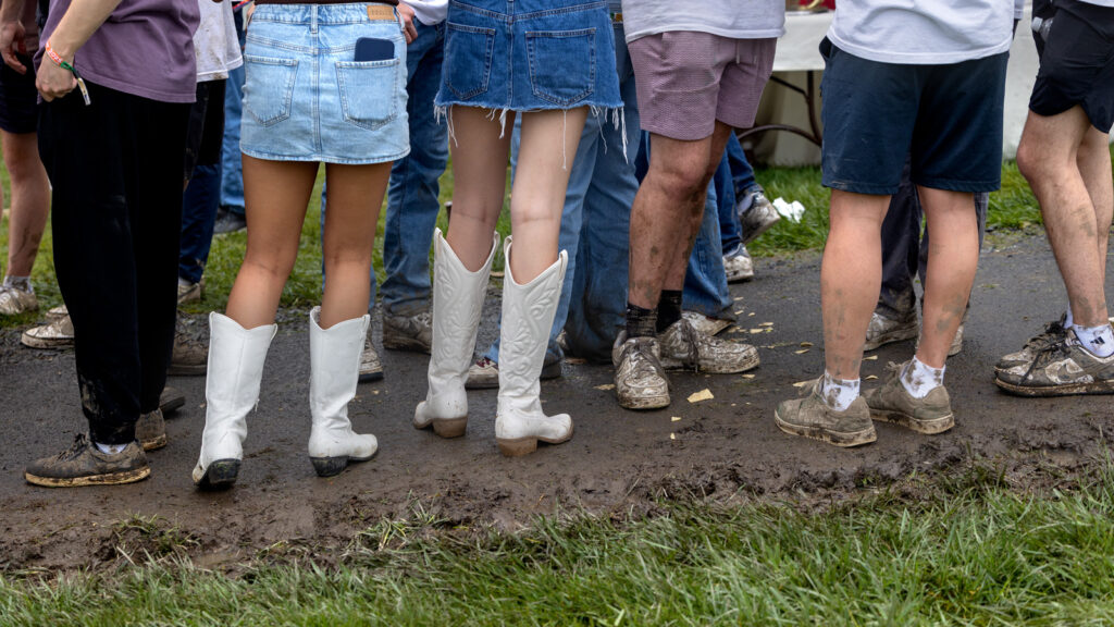 The legs of attendees showing sneakers and boots covered in mud.