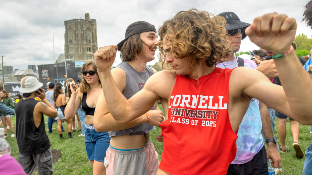 Students dancing and walking around. One student wears a cutoff tank top that says "Cornell University Class of 2025" across the front of it.