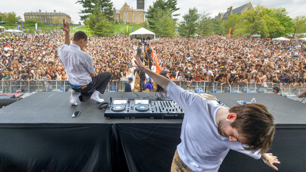 Two men perform on stage in front of a large crowd