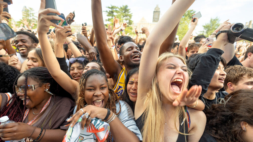 Students in the crowd yell and smile with their hands in the air.