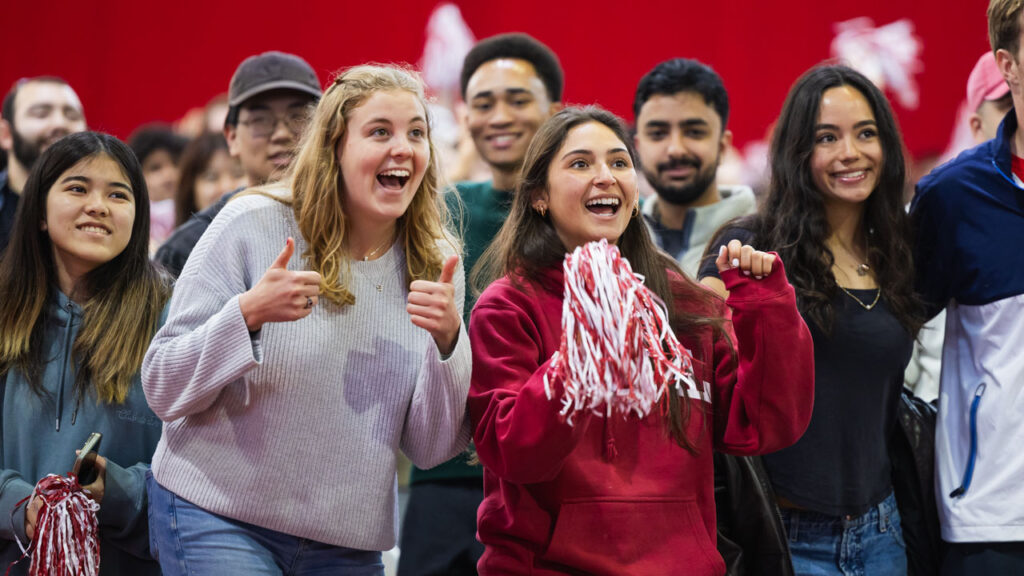 A group of seven seniors smile, some holding red and white pom poms, during 2025 senior convocation.