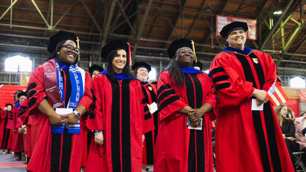 Four Ph.D. graduates from the class of 2025 stand and smile in their academic regalia during the Ph.D. Recognition Ceremony.
