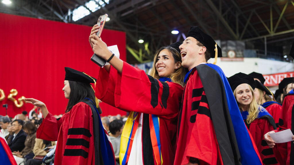 Two class of 2025 Ph.D. graduates wearing their academic regalia smile for a selfie during the 2025 Ph.D. Recognition Ceremony at Barton Hall.