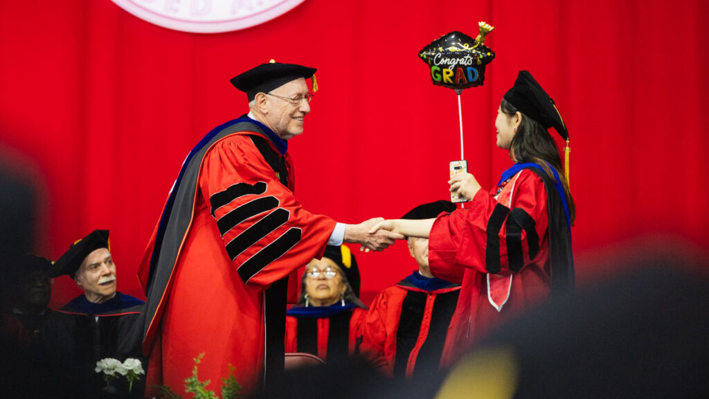 President Mike Kotlikoff, wearing his academic regalia, shakes hands with a Ph.D. graduate, wearing her academic regalia, during the 2025 Ph.D. Recognition Ceremony.