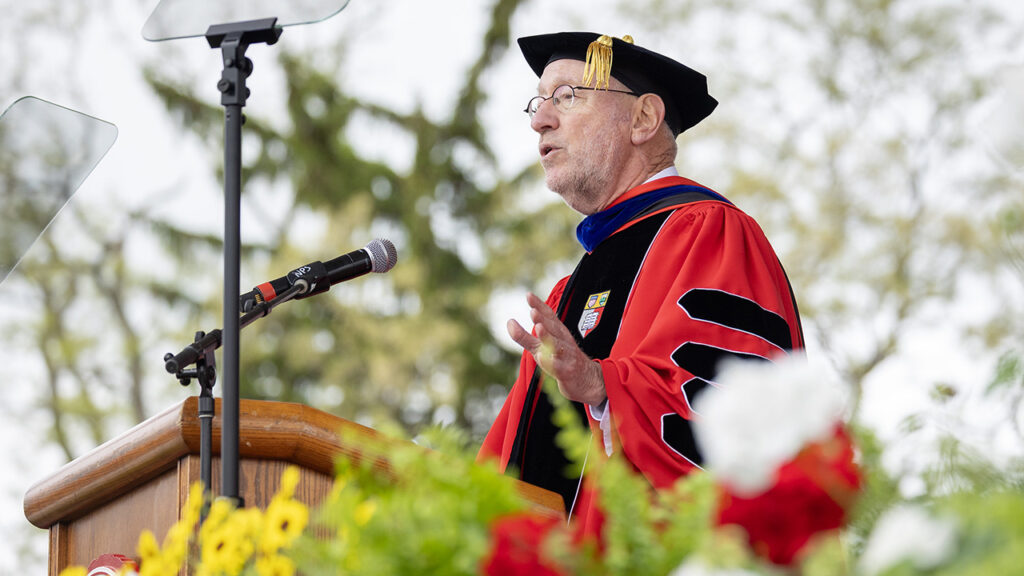 President Mike Kotlikoff, wearing his academic regalia, speaks into a microphone while addressing commencement attendees.