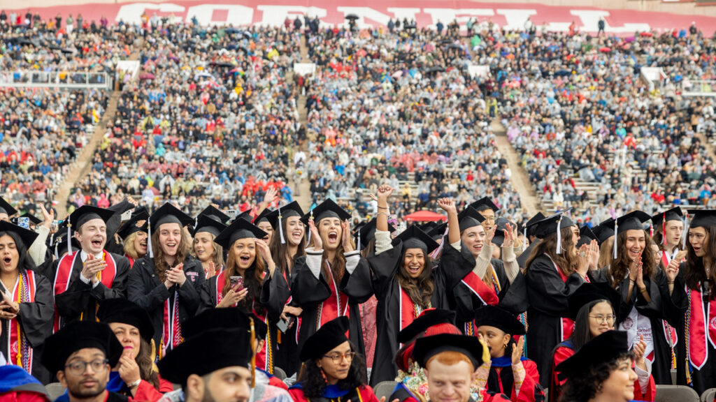 Graduates from the class of 2025 in their academic regalia smile and cheer during commencement at Schoellkopf Field.