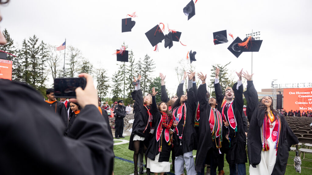 A group of graduates from the class of 2025 toss their caps in their air for a photo after commencement at Schoellkopf Field.