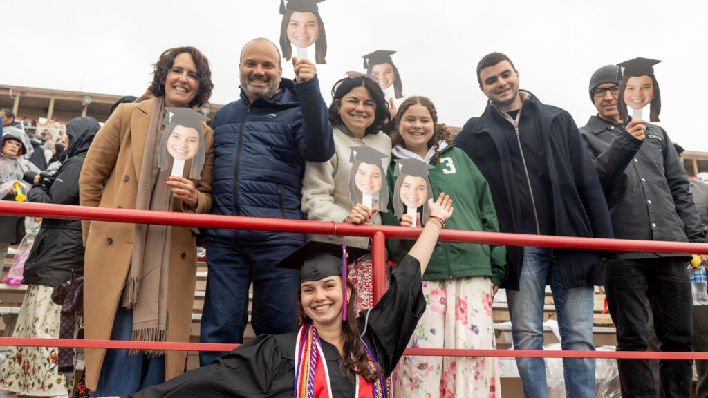 A family smiles for a photo while holding up cut out photos of their graduates head while the graduate smiles in front of them at Schoellkopf Field during commencement.