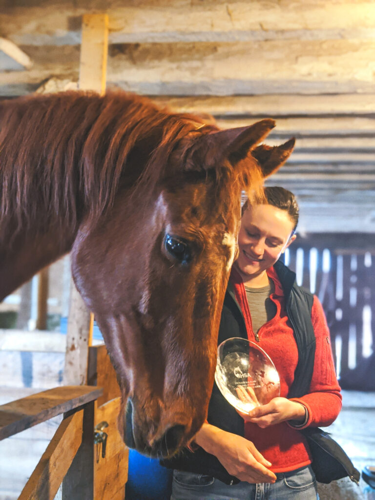 Joanna Novakovic stands with Clifford, the equestrian team's horse, and holds his IHSA Hall of Fame Induction trophy.