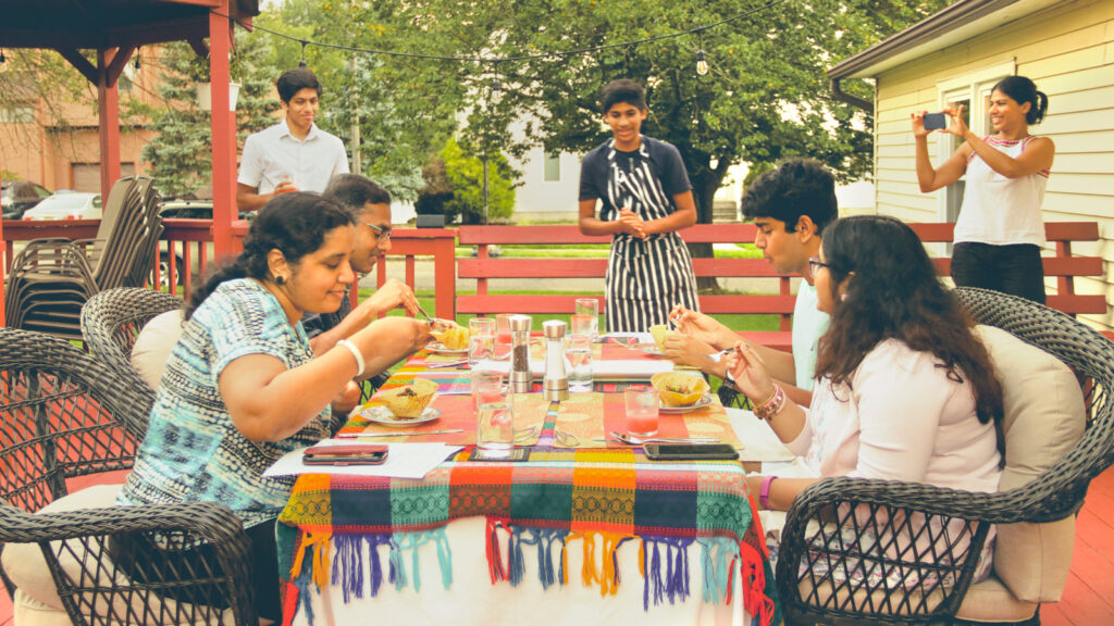 Arnav Kamulkar talks to a table of four diners as they eat at his home restaurant, Fork in the Road, on an outdoor patio.