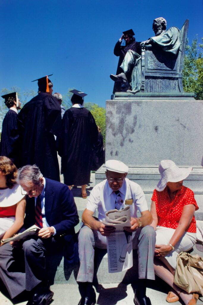 parents read newspapers while sitting below the A.D. White statue as graduates assemble on the Arts Quad in 1984