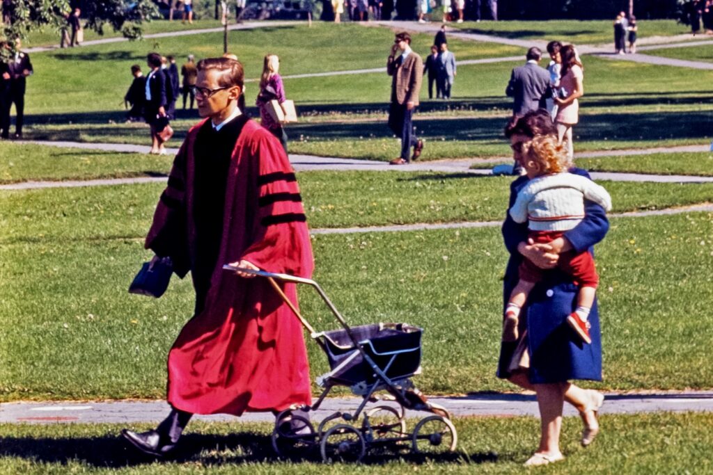 a PhD graduate student crosses the Arts Quad with a baby stroller in tow, followed by a woman carrying a toddler-aged child during Commencement Weekend 1969