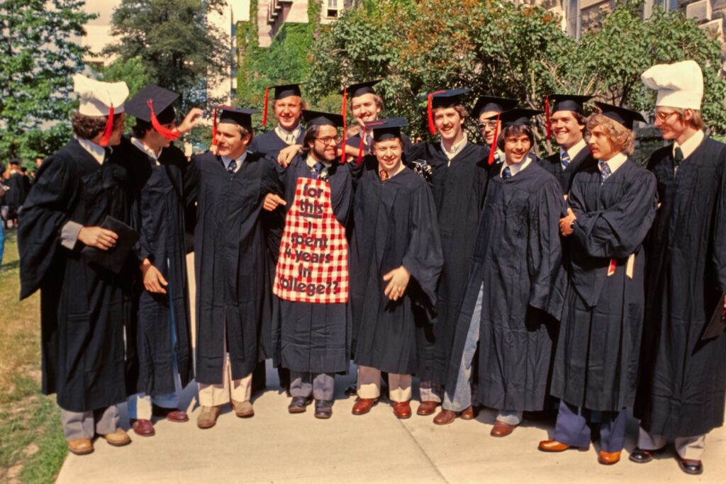 graduates of the School of Hotel Administration gather for a group photo, with some wearing chef's hats and one sporting an apron stating "for this I spent 4 years in college??" during Commencement Weekend 1977