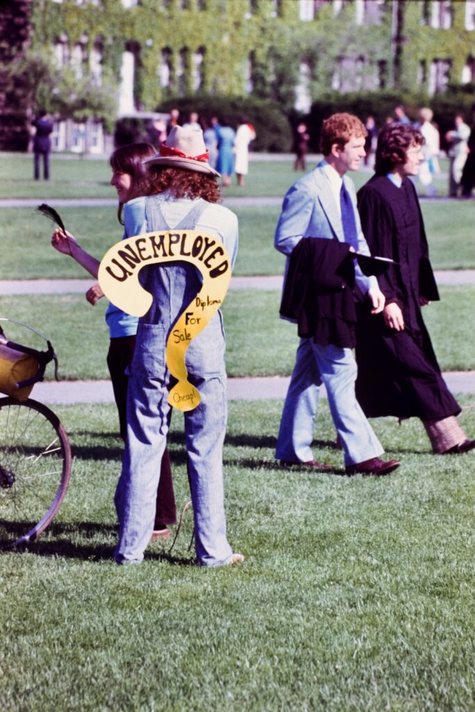 a student on the Arts Quad during a Commencement Weekend in 1976 wears a question-mark-shaped sign that says "Unemployed: Diploma for sale – cheap!"
