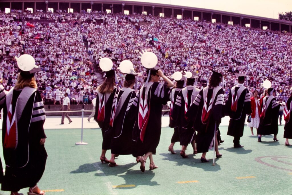 graduates in the College of Veterinary Medicine hold inflated gloves on their mortarboards while processing into Schoellkopf Stadium in 1986