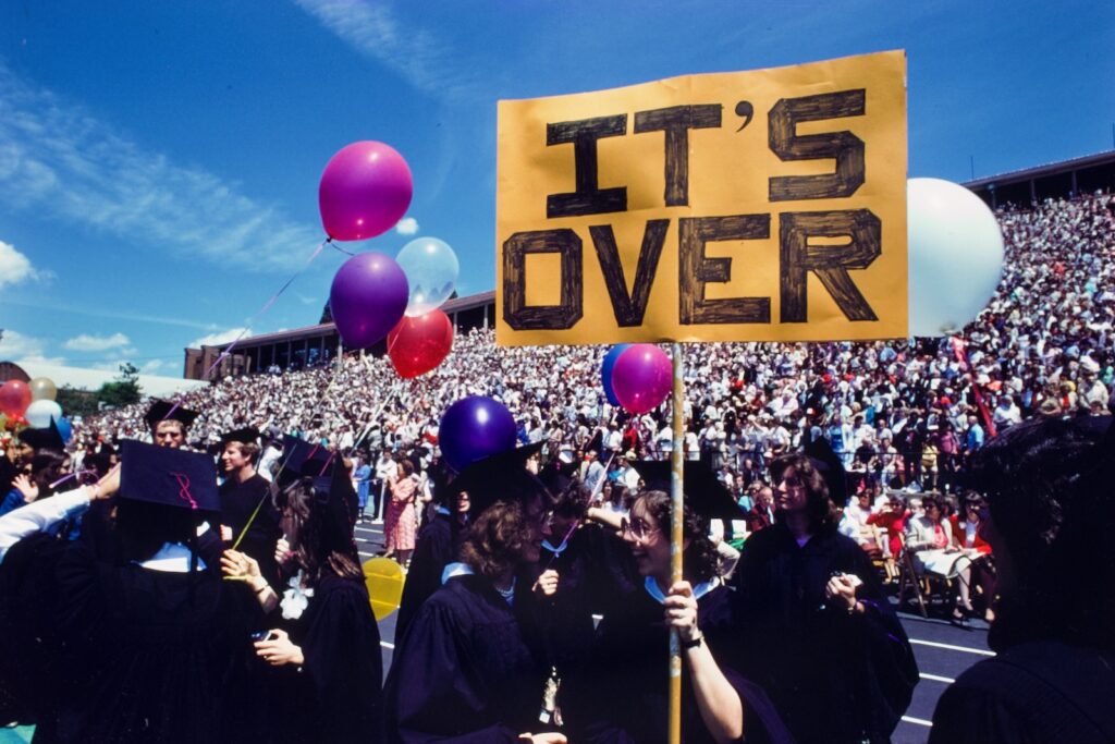 graduating seniors in Schoellkopf Stadium in 1990 hold balloons and a sign that states "It's Over"