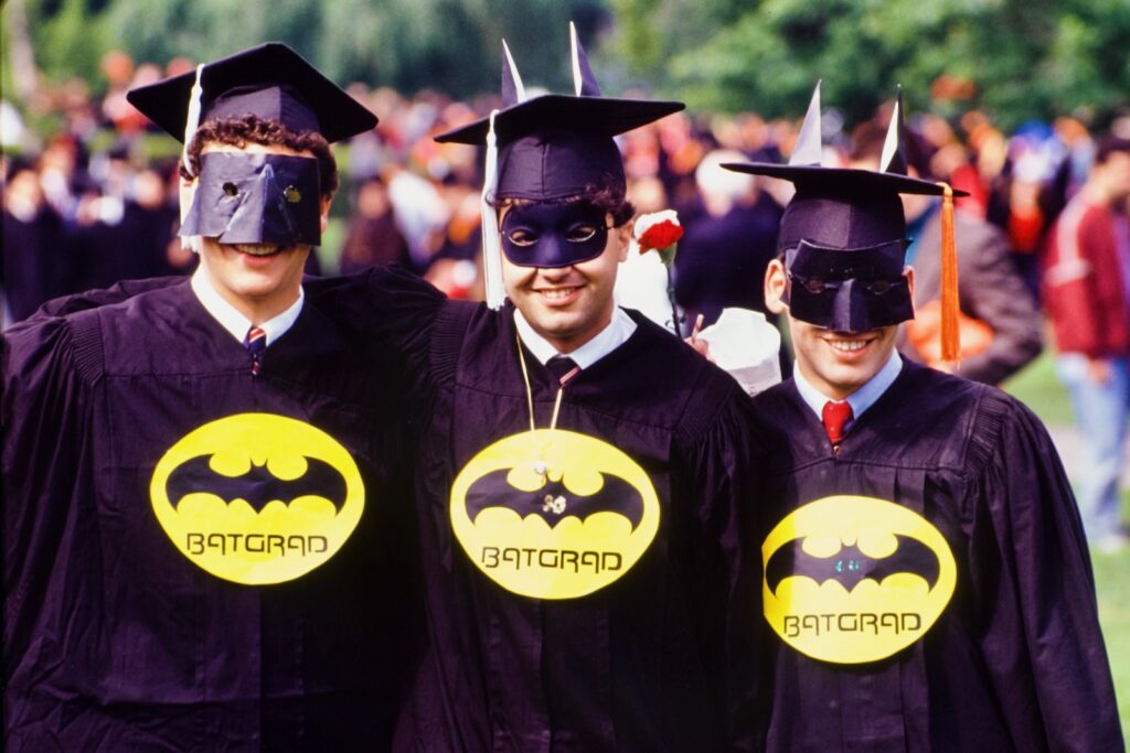 three graduating seniors sport "BatGrad" emblems and masks during Commencement Weekend 1990