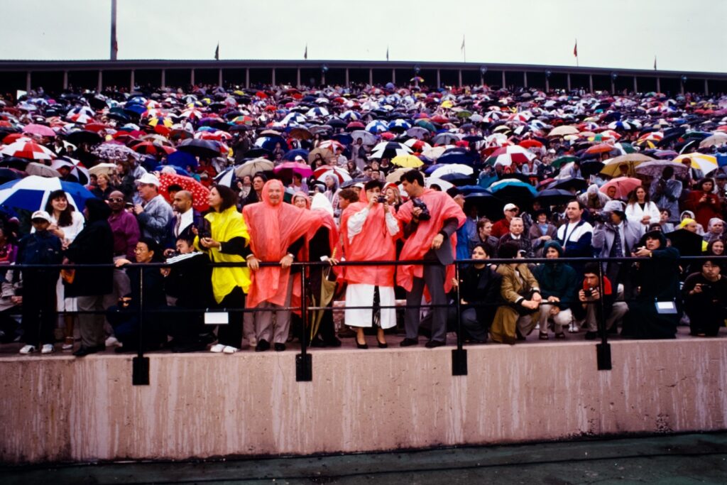 Family members and friends wear ponchos and hold umbrellas in Schoellkopf Stadium during a rainy portion of Commencement in 1997
