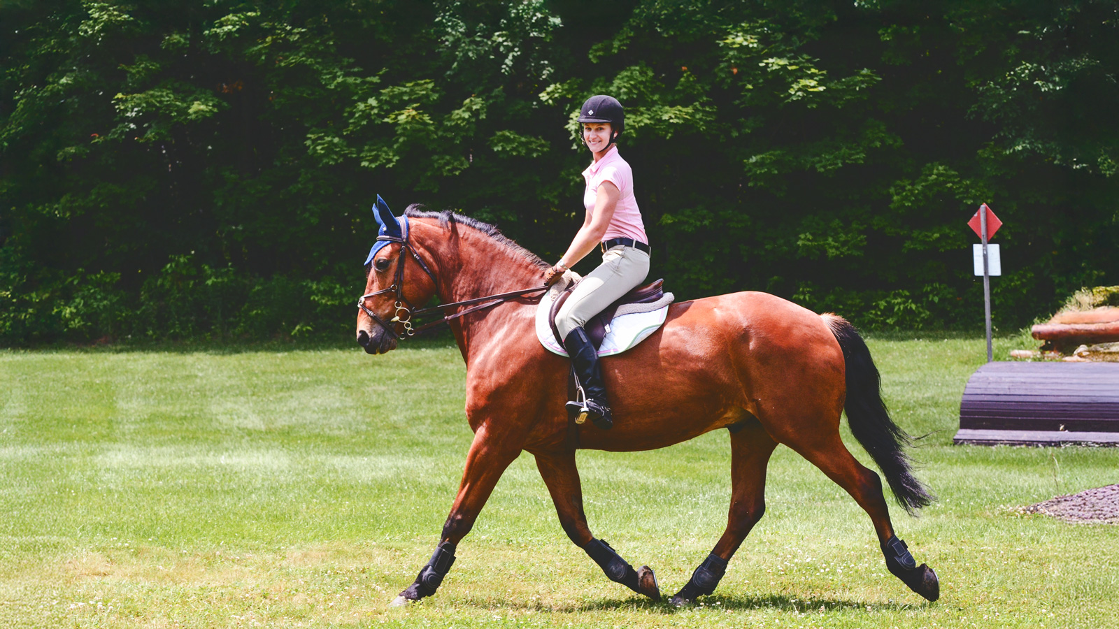 Joanna Novakovic riding a horse through the grass and smiling.