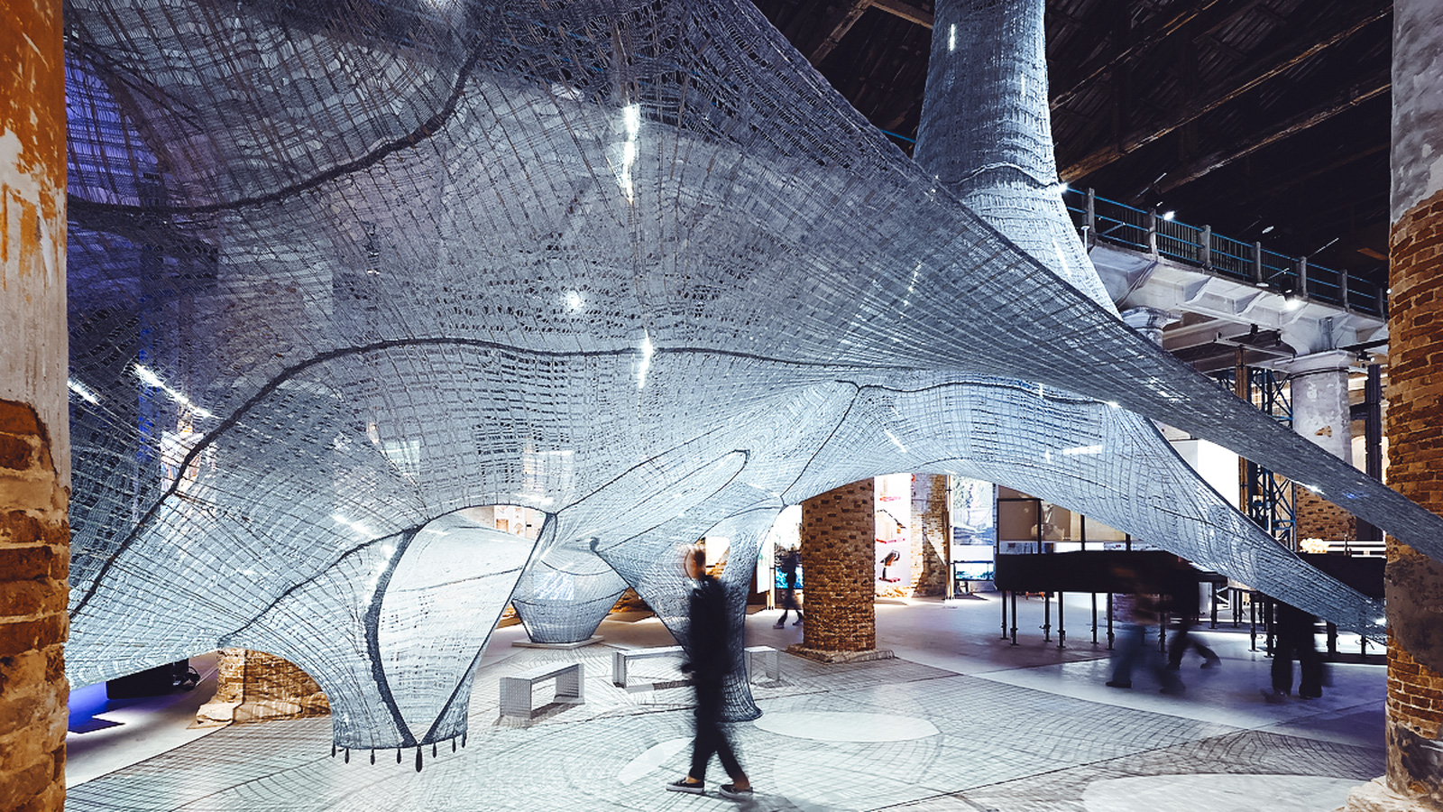 "Necto" depicts fiber panels stretched across brick columns. A man is walking in front of them.