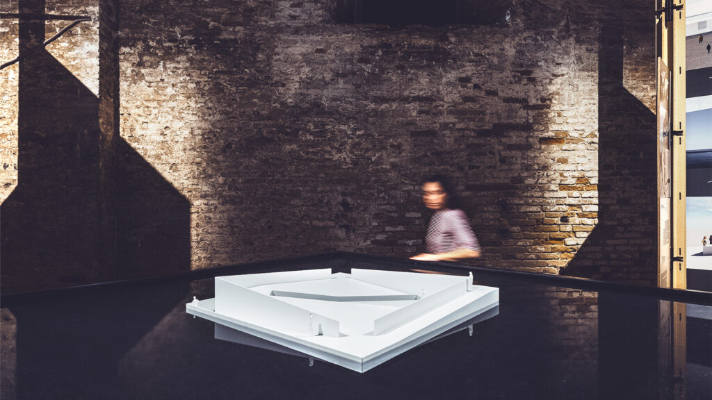 "AquaPraça" on display. It is a floating white square platform surrounded by water. A woman is walking past it.