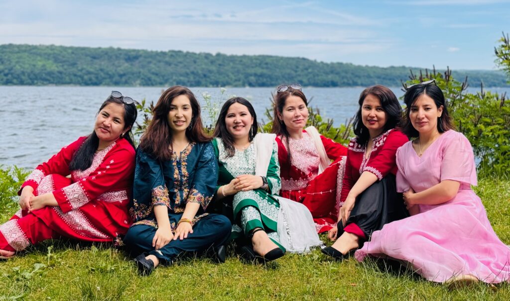 Six women in traditional Afghan clothing sitting by a lake