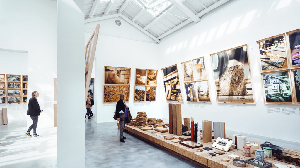 A view of "Internalities: Architectures for Territorial Equilibrium" in the Spanish Pavilion. There is a low wooden platform with architectural models and large color photos of building materials on the wall.