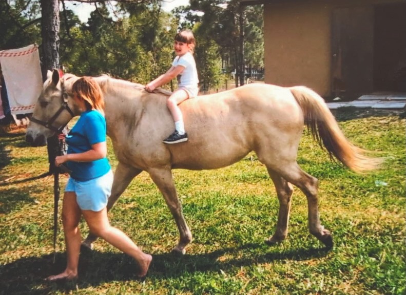 A young Joanna Novakovic sits on a horse that is guided by her aunt.