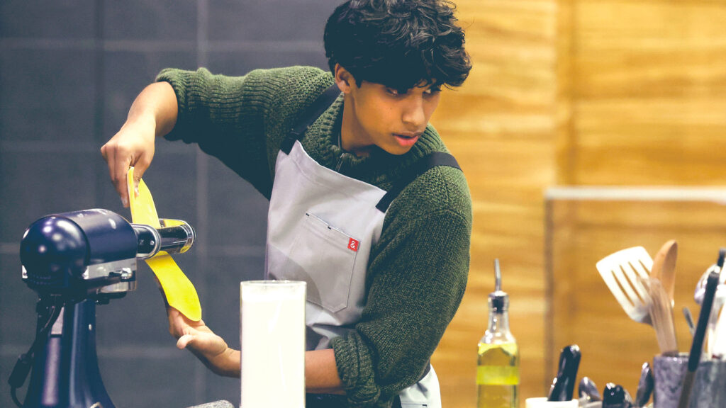 Arnav Kamulkar flattens pasta dough using a kitchen aid mixer attachment during a challenge in Next Level Chef.