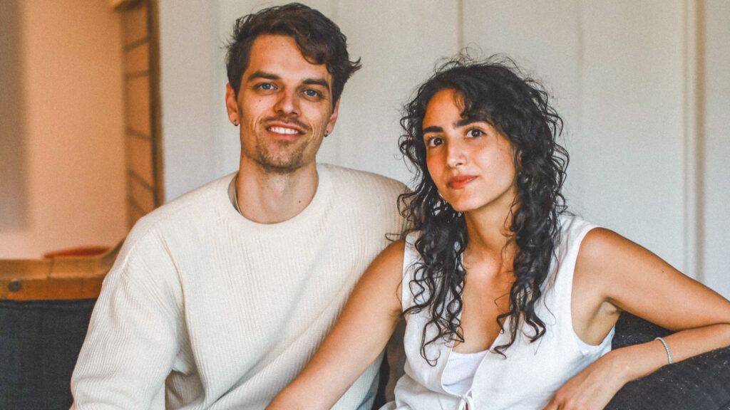 Quinn Cox and Lilia Karimi sit on a sofa together and smile.