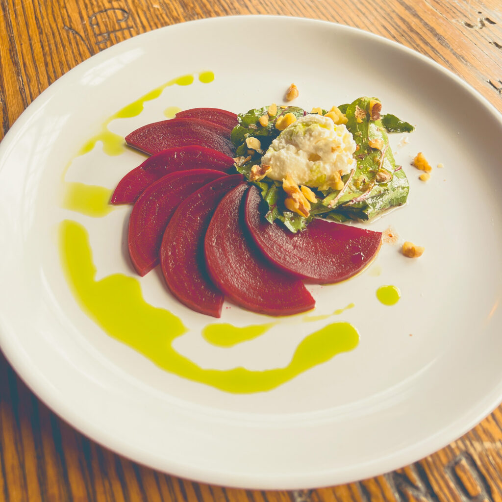 Cherry braised beets, homemade ricotta, dill oil, and cherry gastrique on a white plate.