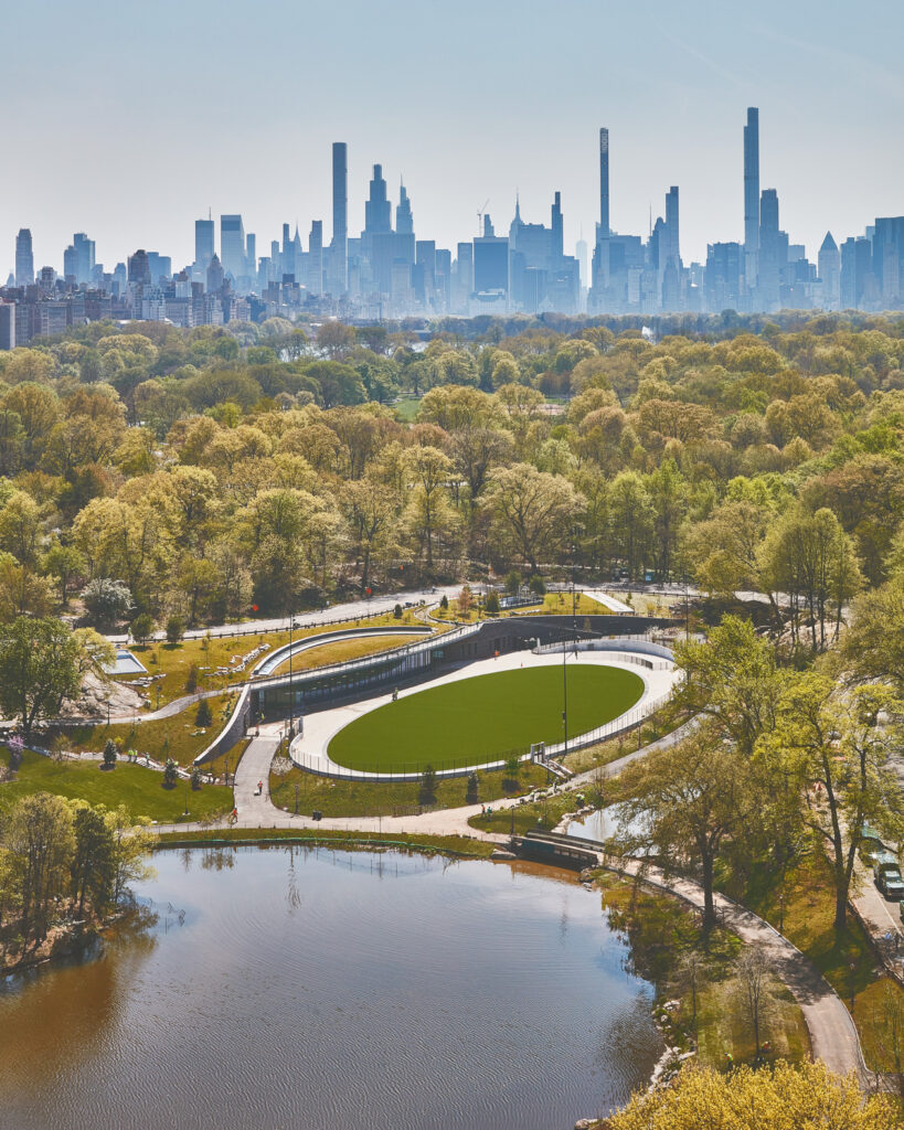 vertical aerial shot of the Harlem Meer, the finished project site, and Central Park and the Manhattan skyline in the background