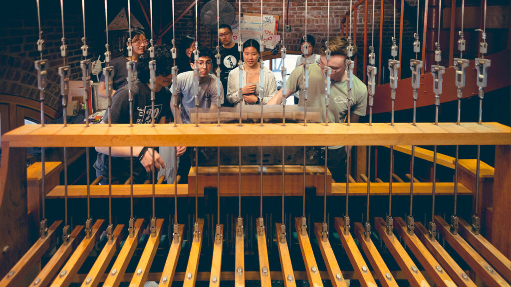 New chimesmaster Alex Gardocki and another chimesmaster perform a duet on the chimes in McGraw Tower while other chimesmasters watch them perform.