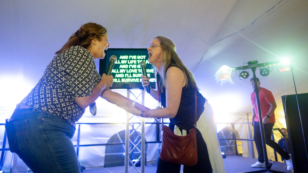 Two women perform karaoke during the tent parties on the Arts Quad