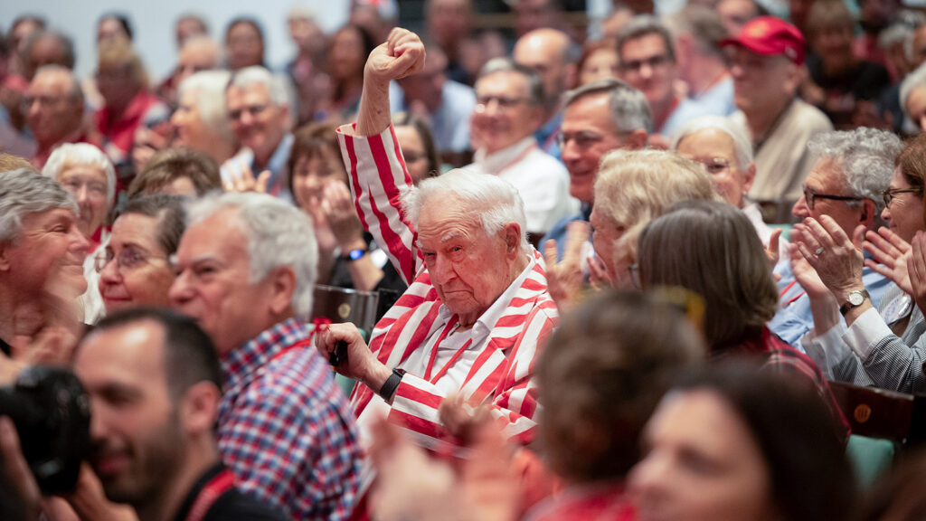 a man in a red and white striped jacket raises a first during the State of the University Address