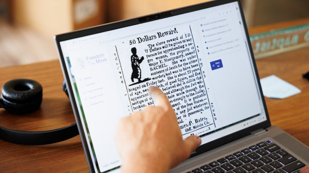 A finger pointing at a laptop screen showing an ad offering "50 Dollars" as the reward for a fugitive slave
