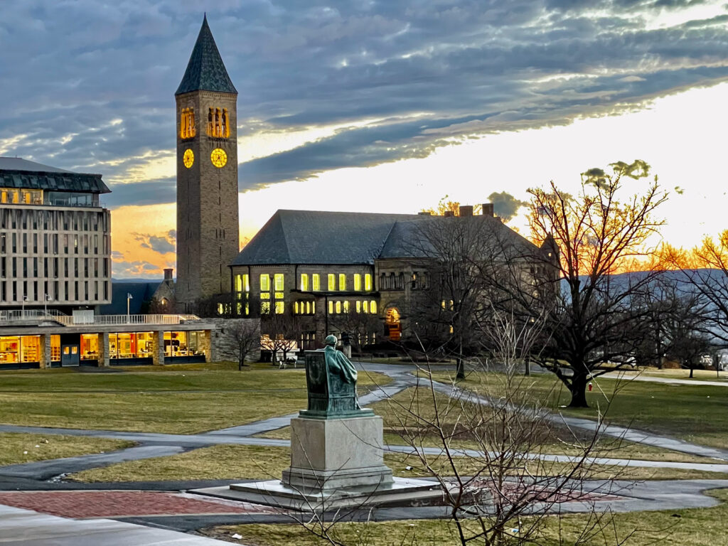 view of the Andrew Dickson White statue, the Arts Quad, McGraw Tower, and surrounding buildings against a sunset sky