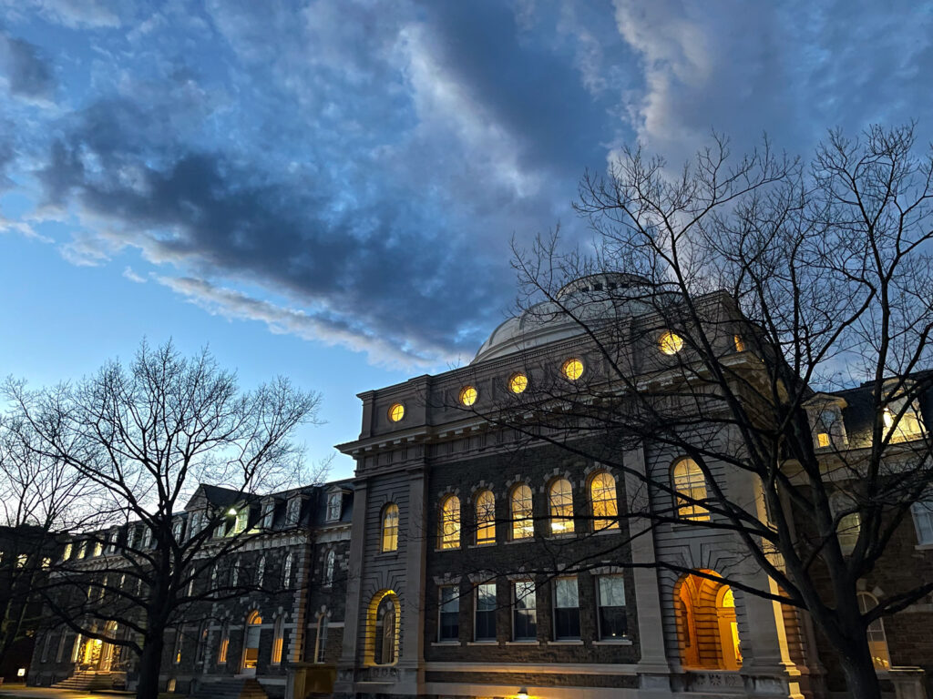 Lights shine in the windows of Sibley Hall with a blue, cloud-streaked sky in the background during the evening
