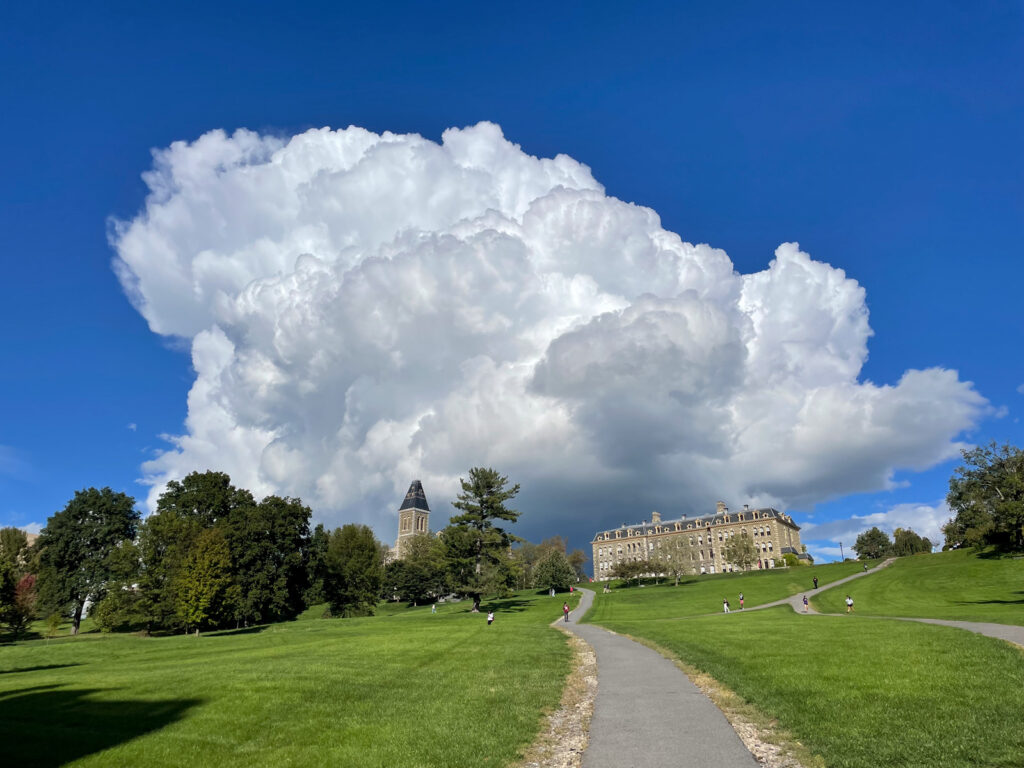 A view looking up a pathway from the bottom of the Slope with Morrill Hall at the top and a bright blue sky with puffy, white clouds