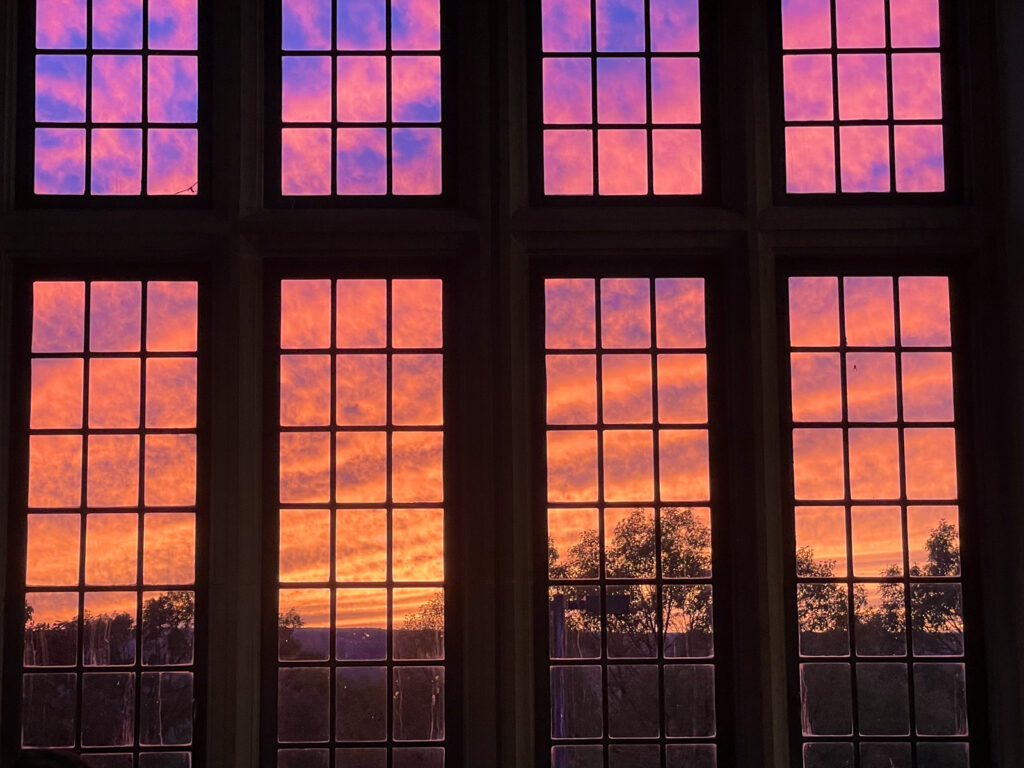 View of a sunset, featuring hues of bright yellow, orange, and purple, through rectangular window panes in Willard Straight Hall