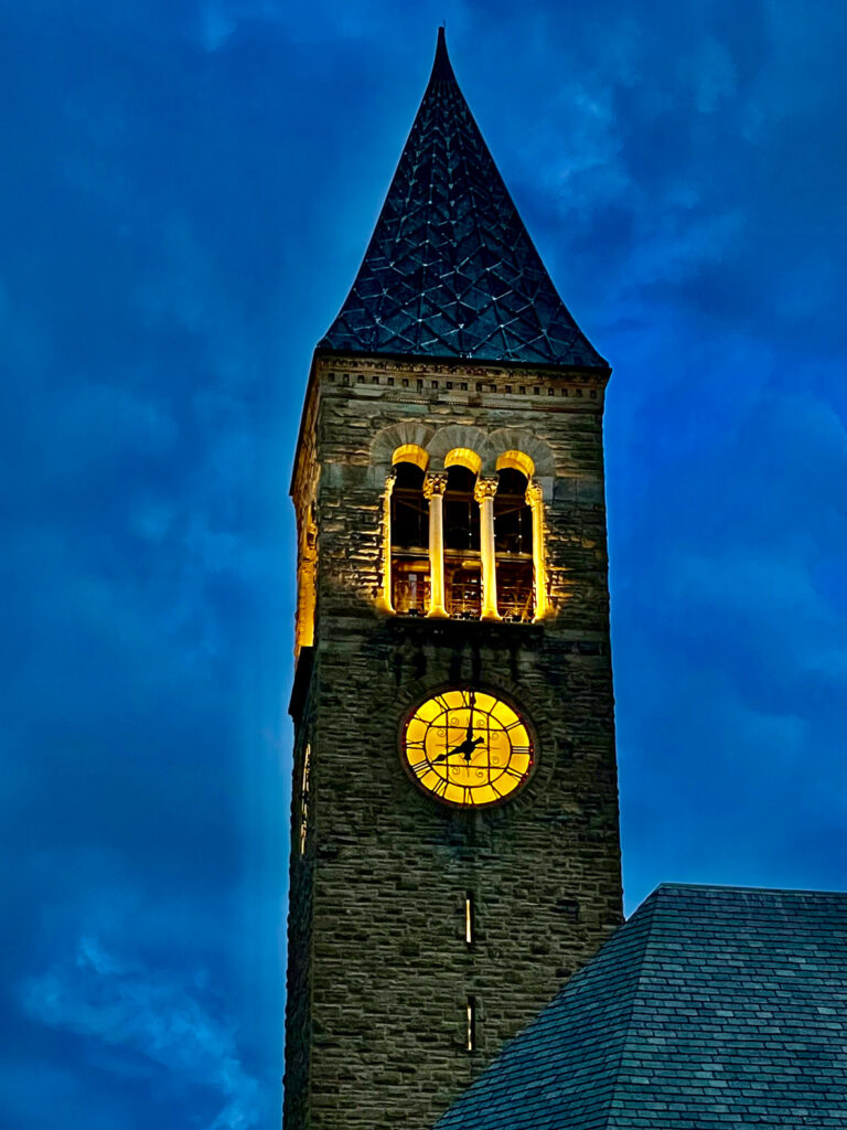 The top of McGraw Tower with lights illuminating the building against a dark blue sky