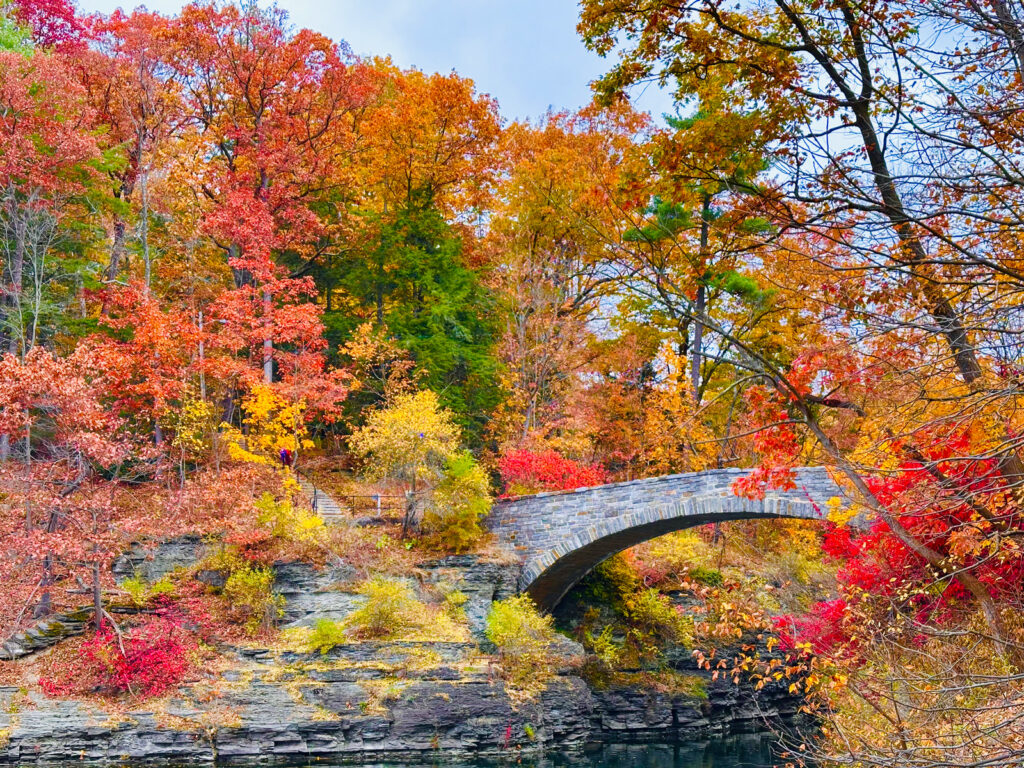 the stone arch bridge over Beebe Lake, surrounded by fall foliage in hues of orange, red, and yellow