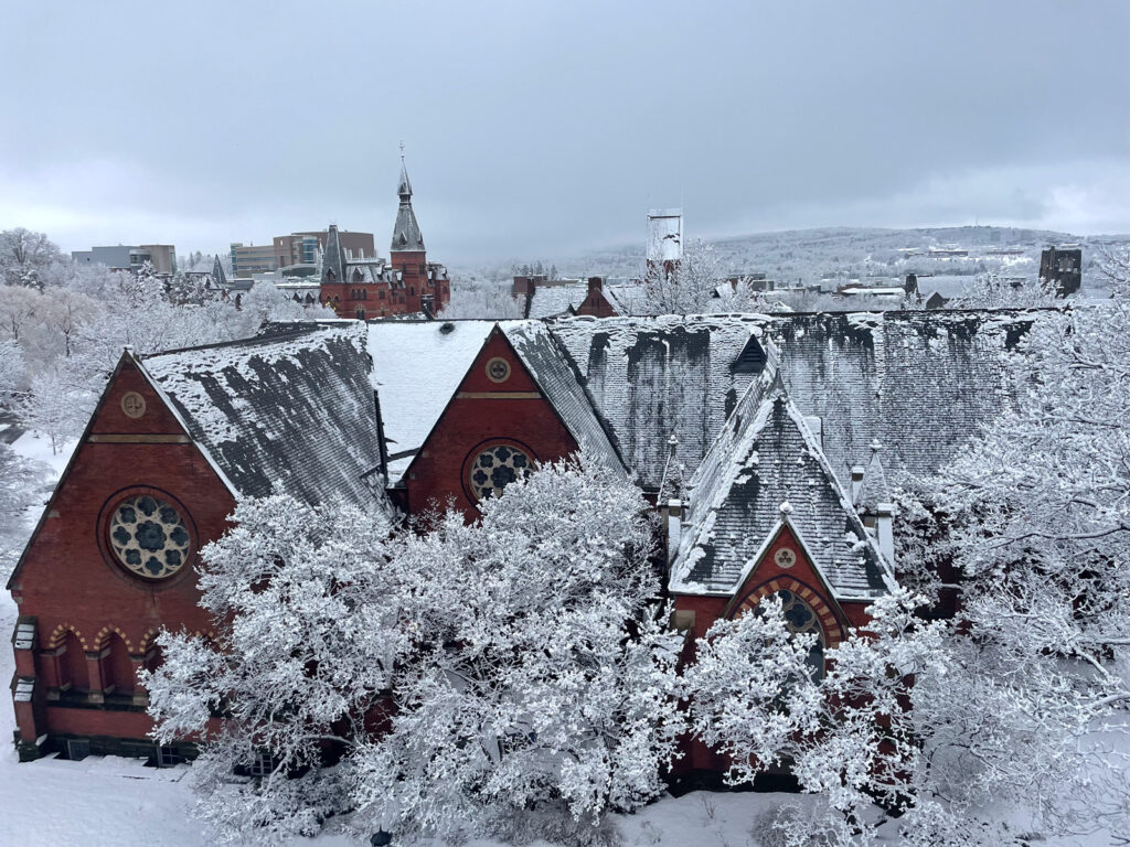 a snow-frosted Sage Chapel and its surrounding trees, with Sage Hall and other campus buildings in the background