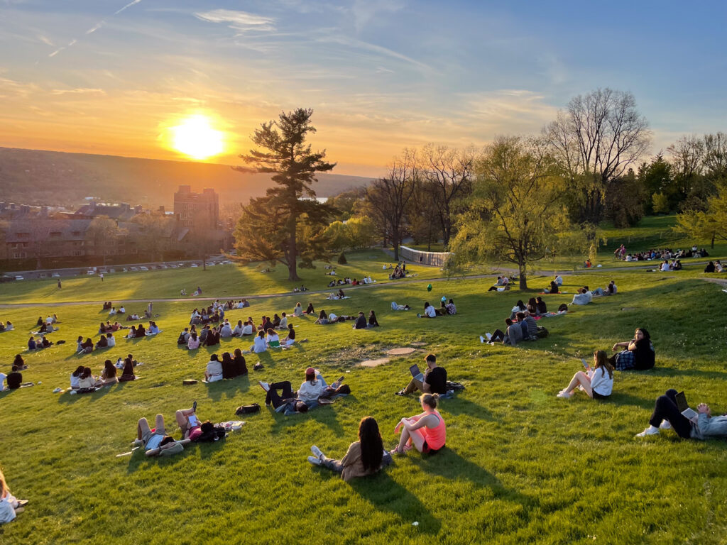 Dozens of students sit on the Sope and watch a sunset