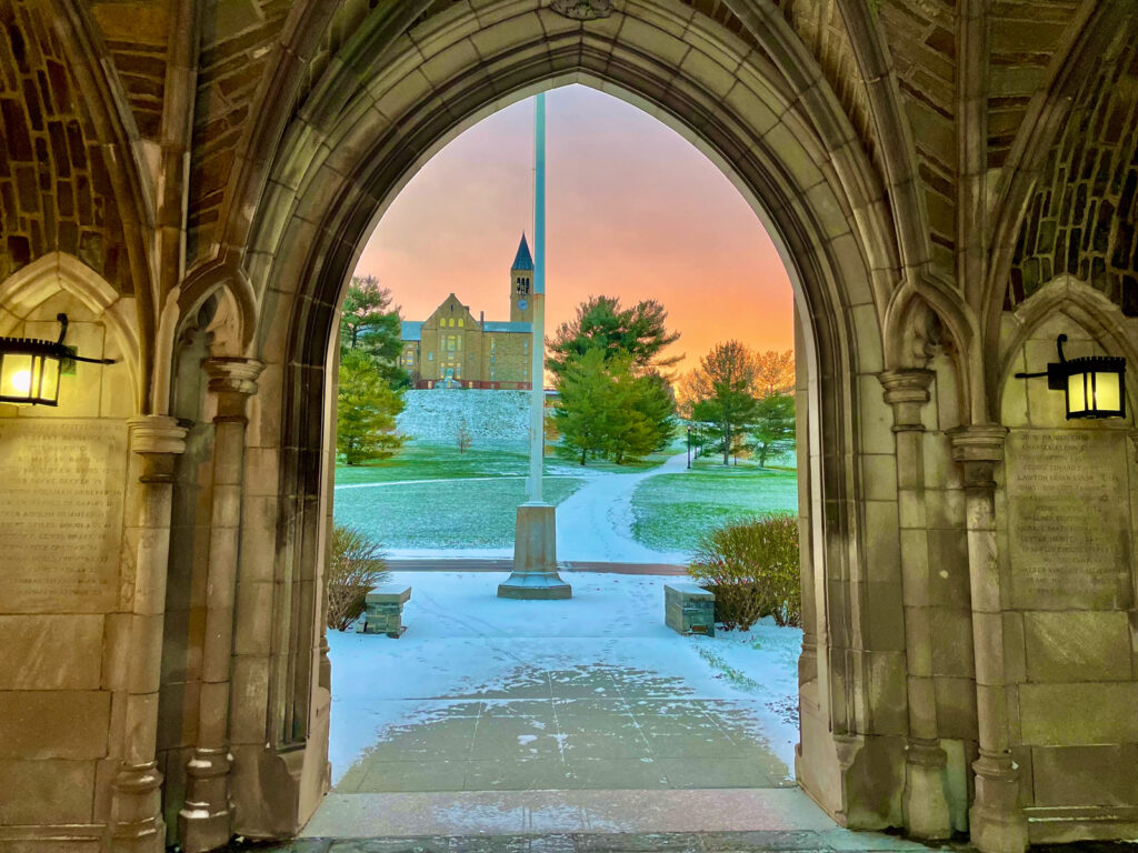 view from the arched entryway of the War Memorial, looking out at the Slope, McGraw Tower, and a pink and yellow sky during sunset